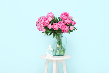 Vase of pink peonies with figurine on chair near blue wall