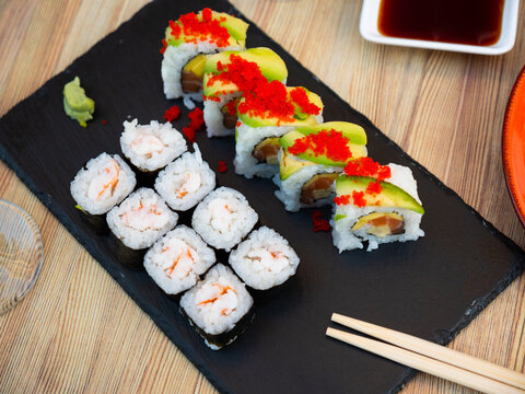 Appetizing uramaki with salmon, mango and cucumber topped with avocado slices and tobiko and hosomaki with tiger shrimp traditionally served with wasabi and soy sauce. Japanese cuisine