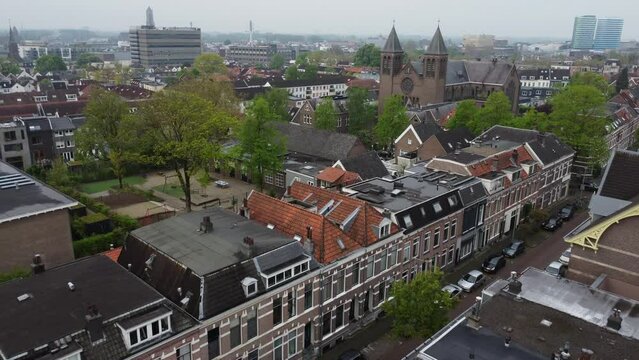 Aerial view of Arnhem neighborhood flying towards church - Drone footage of the Dutch city of Arnhem. Flying over the neighborhood Graaf Ottoplein E.O. towards a church. In the background highrises in