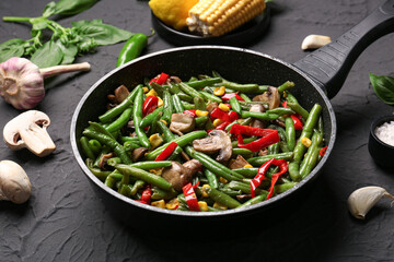 Frying pan with different vegetables on black background