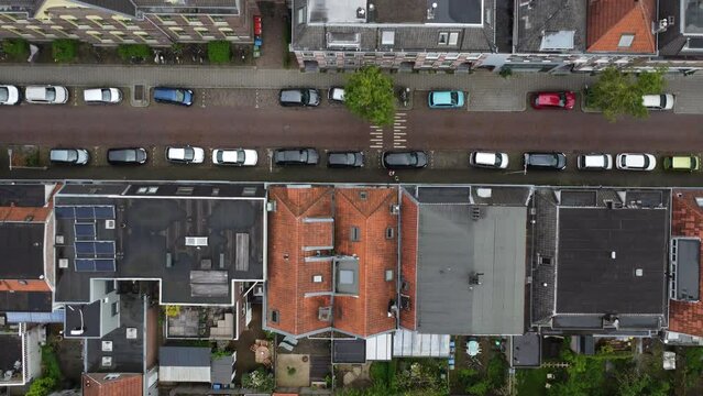 Aerial view looking top down at a residential area of Arnhem, a city in the Netherlands. The drone flies over a mix of 1890/1900's buildings, modern structures, gardens, a schoolyard and parking area.