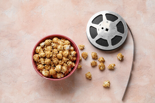Bowl with tasty popcorn and film reel on pink background