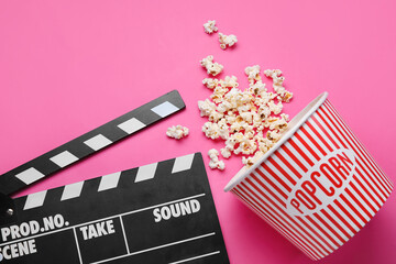 Bucket with tasty popcorn and clapperboard on pink background