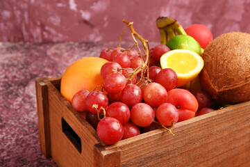 Wooden box with different fresh fruits on purple background