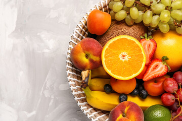 Wicker bowl with different fresh fruits on grey background