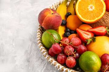 Wicker bowl with different fresh fruits on grey background