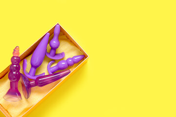 Gift box with different dildos on yellow background