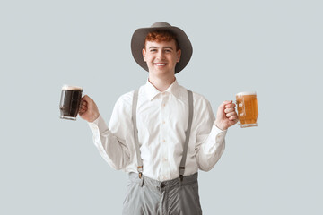 Young man in traditional German clothes with beer on light background