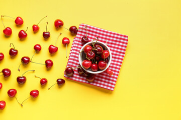 Cup with sweet cherries on yellow background