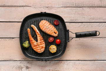 Frying pan with tasty grilled salmon steaks and vegetables on light wooden background