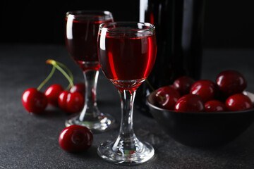 Glasses with sweet cherry liqueur on black background