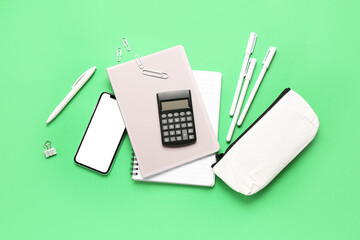 Modern calculator with mobile phone and stationery on green background