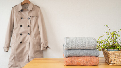 たたまれたセーターとトレンチコート｜洗濯物・衣替えイメージ