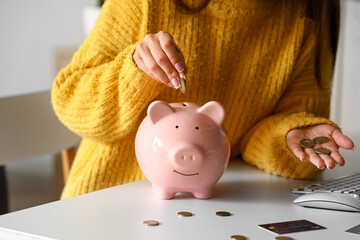 Young woman putting coin in piggy bank at home, closeup