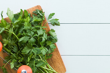 Bundle of fresh flat leaf parsley on wooden chopping board with mezzaluna herb knife on the side, photographed overhead with copy space on the side (Selective Focus, Focus on leaves on top) - Powered by Adobe