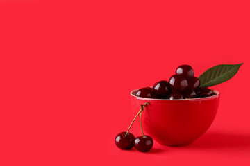 Bowl with sweet cherries and leaf on red background