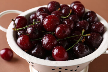 Colander with sweet cherries on brown background