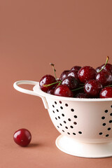 Colander with sweet cherries on brown background