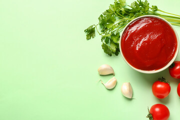 Bowl with tomato paste and fresh vegetables on green background
