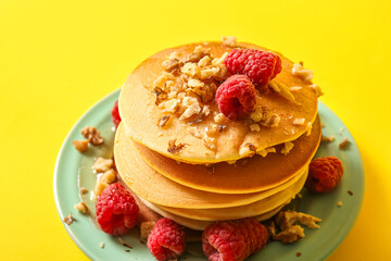 Plate of tasty pancakes with raspberries on yellow background