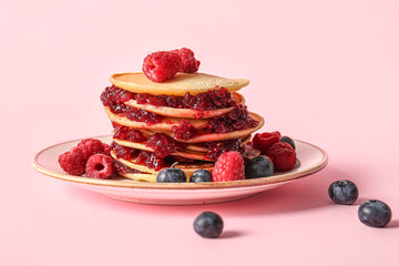 Plate of tasty pancakes with raspberries and blueberries on pink background