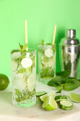 Glasses of mojito cocktails with cucumber, lime and mint on green background