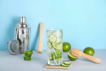 Glass of fresh cucumber mojito with bartender tools on blue background
