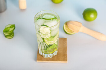 Glass of fresh cucumber mojito on light background