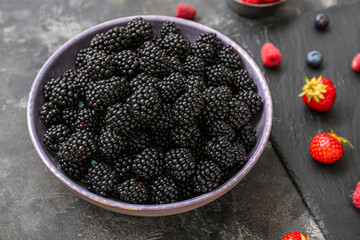 Bowl with fresh blackberry on grey background, closeup