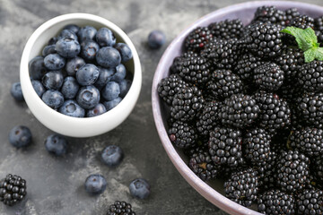 Bowls with fresh blackberry and blueberry on grey background, closeup
