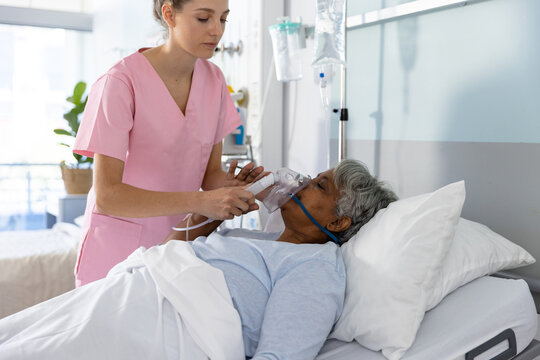 Diverse female doctor and senior female patient wearing oxygen mask at hospital