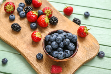 Board with different fresh berries on color wooden background, closeup