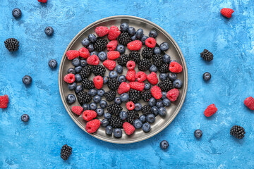 Plate with different fresh berries on blue background