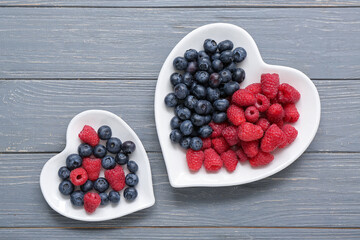 Plates with different fresh berries on grey wooden background