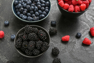 Bowls with fresh raspberry, blueberry and blackberry on black background, closeup