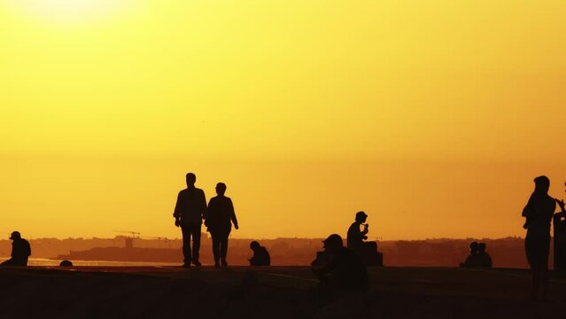 Black silhouettes of people on the hill at sunset - a couple walking holding hands