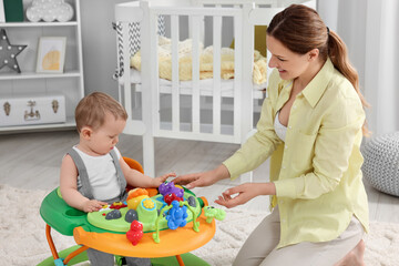 Mother and her little son spending time together at home. Cute baby making first steps with toy...