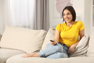 Happy woman watching TV on sofa indoors, space for text
