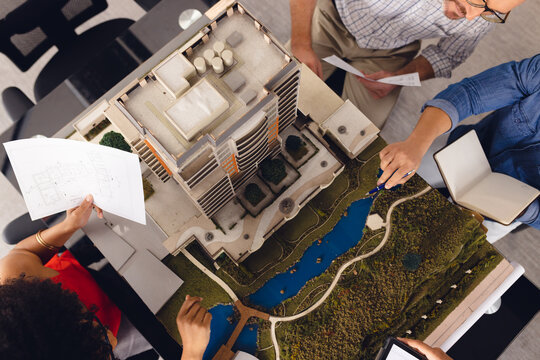Diverse business people looking at architectural plans and model, discussing work at office