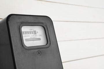 Black electric meter on white wooden wall, closeup with space for text. Measuring device