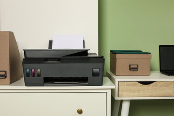 Modern printer with paper on white chest of drawers near stylish workplace indoors