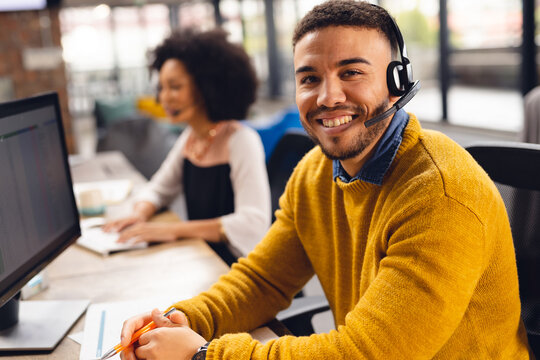 Portrait of happy biracial businessman using phone headset and smiling at office