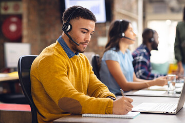 Diverse business people sitting at desks and using phone headsets at office