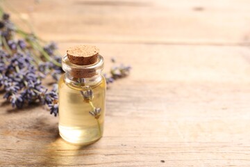 Bottle of essential oil and lavender flowers on wooden table, space for text