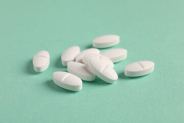 Obraz na płótnie Canvas Pile of white pills on green background, closeup