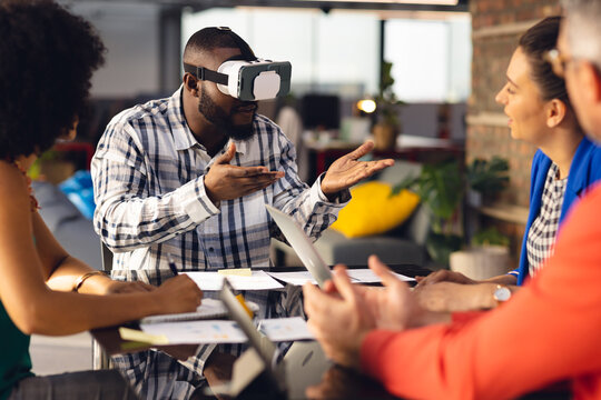 Diverse casual business colleagues in discussion, using vr headset at office meeting