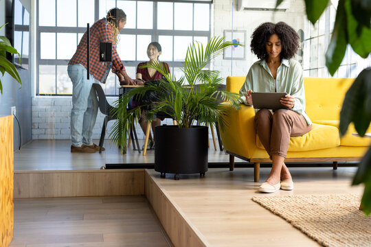 Diverse casual businesswoman using tablet and colleagues discussing work at office