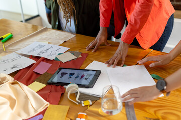 Midsection of diverse fashion designers using tablet and discussing design drawings at studio