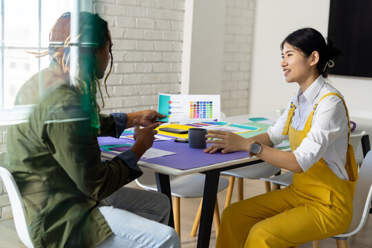 Diverse male and female creative colleagues sitting at table discussing colour palette in meeting