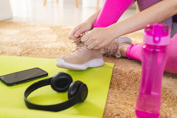 Caucasian woman tying shoes on carpet with yoga mat, smartphone and headphones